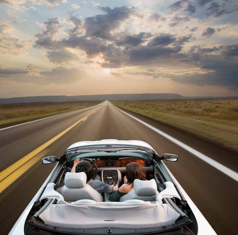 Couple driving down an open road in a convertible sports car.