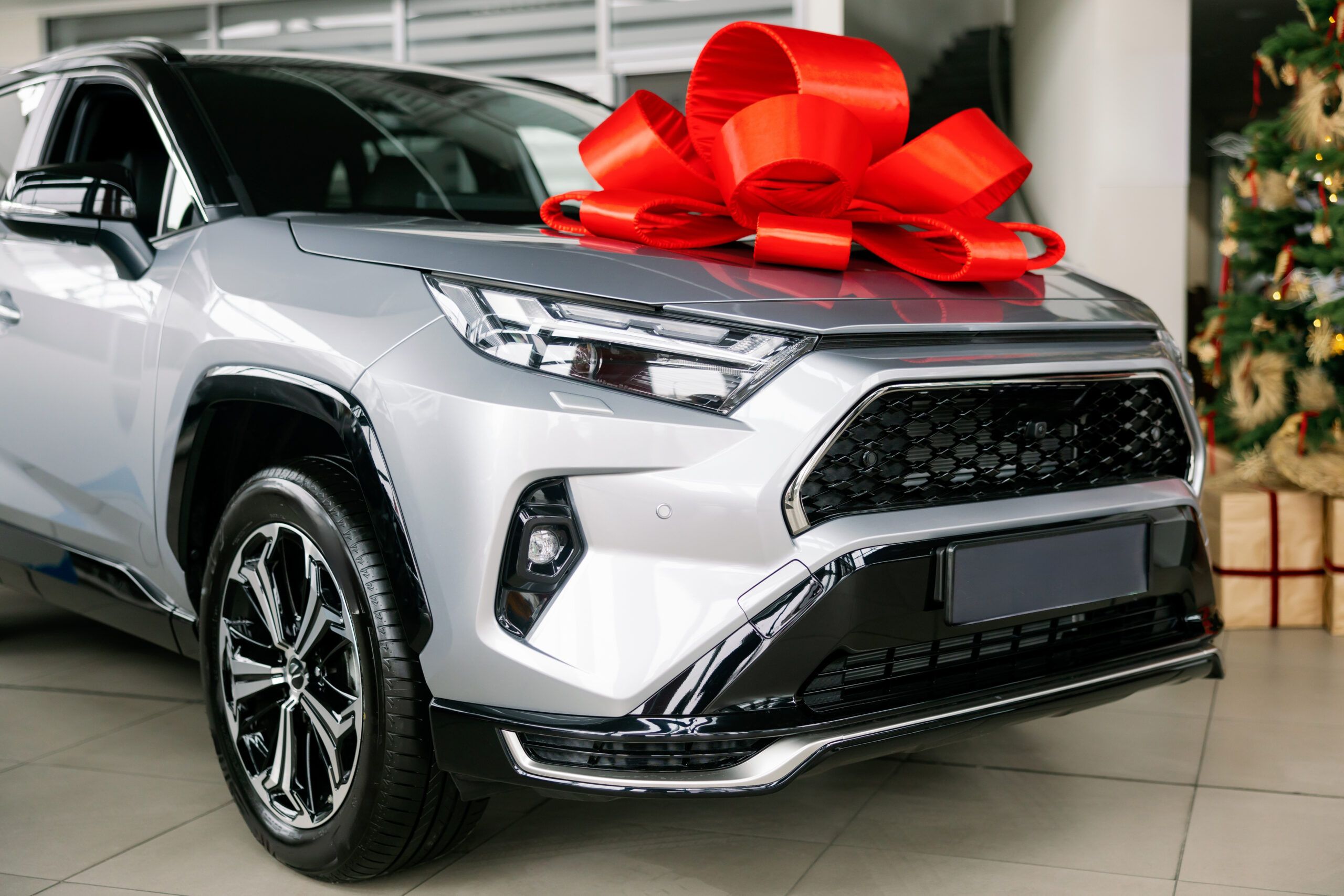Silver car with red bow parked in dealership showroom