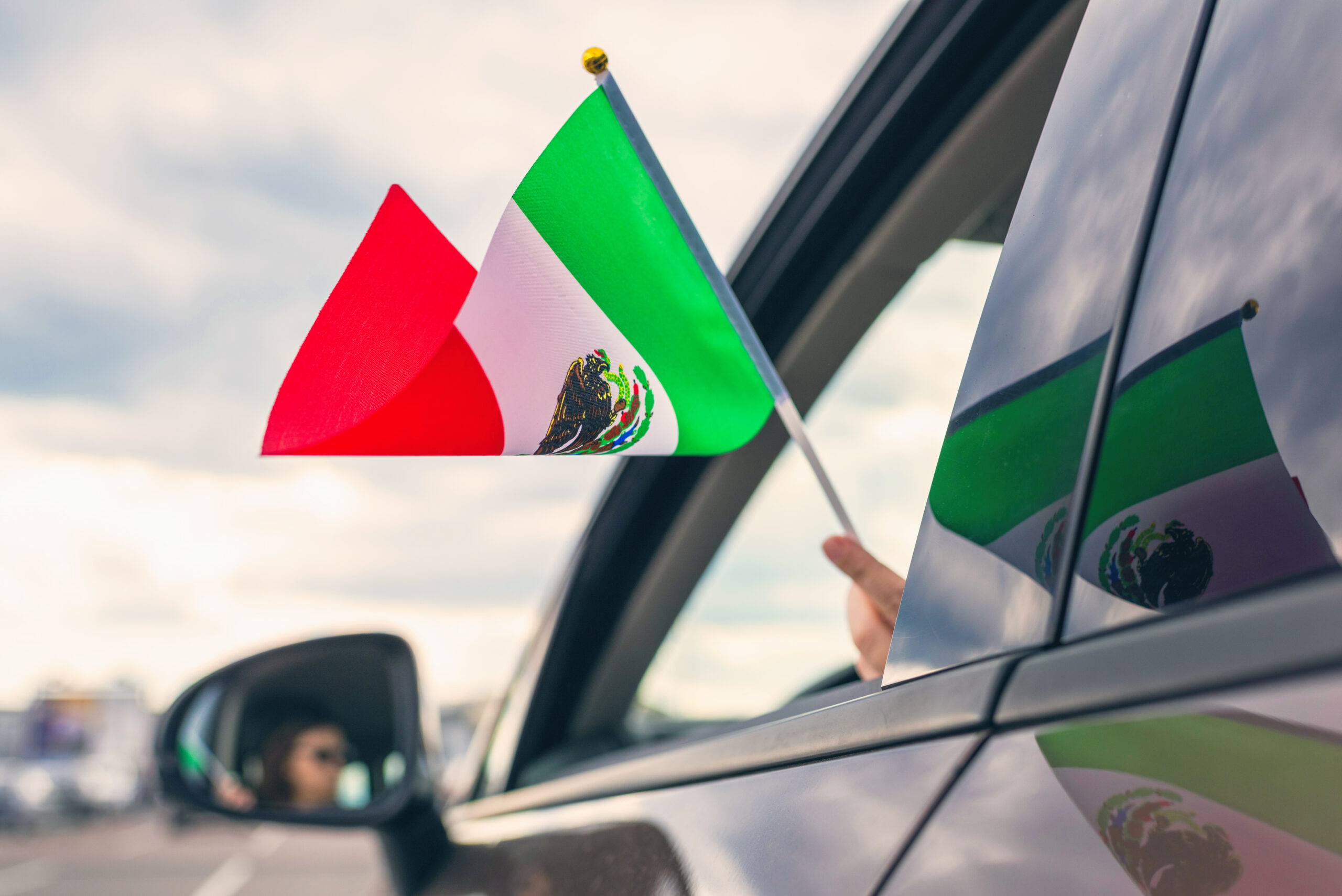 Girl holding a Mexican flag from the open car window.